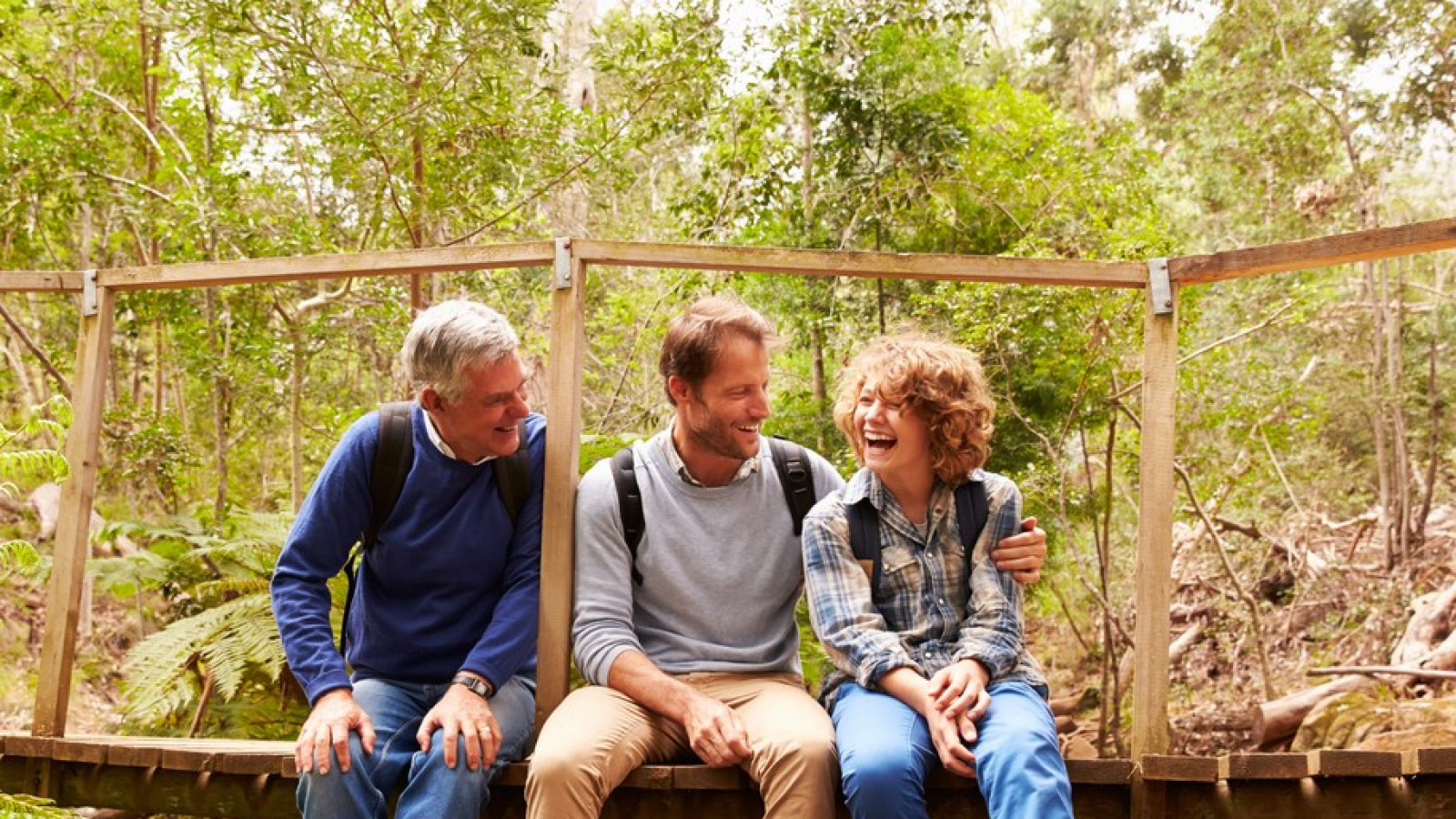 Grandfather, father and son sitting on a bridge in a forest